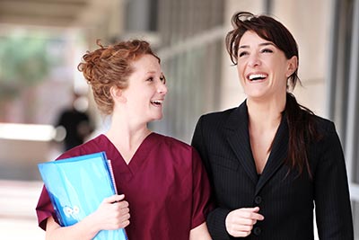 Female Doctor and Nurse laughing in Hospital Corridor.